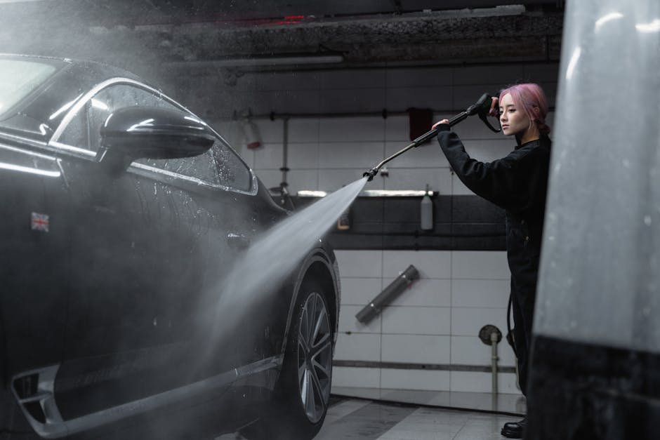 Woman power washing a black car in an indoor garage using a high-pressure washer.